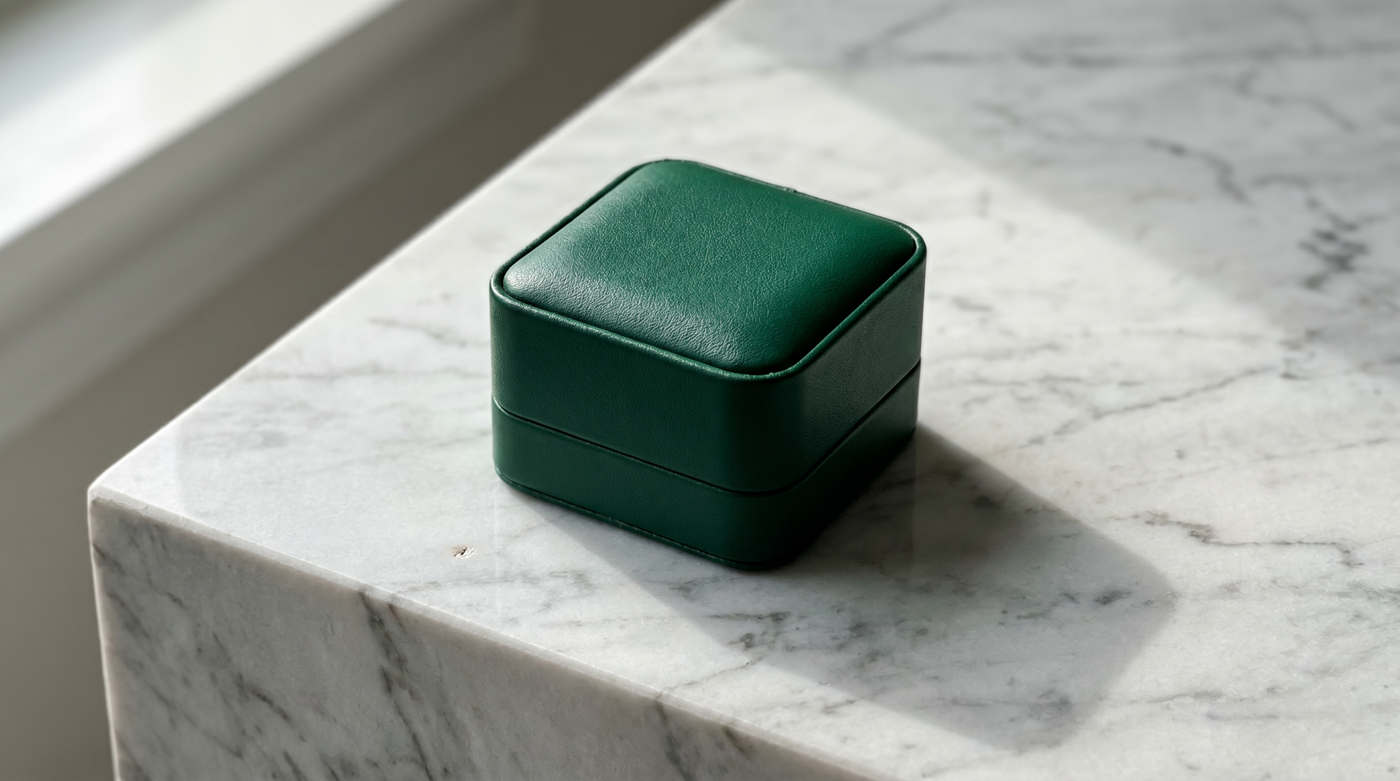 Emerald Green Ormelya Signature engagement ring box closed on veined marble in soft window light